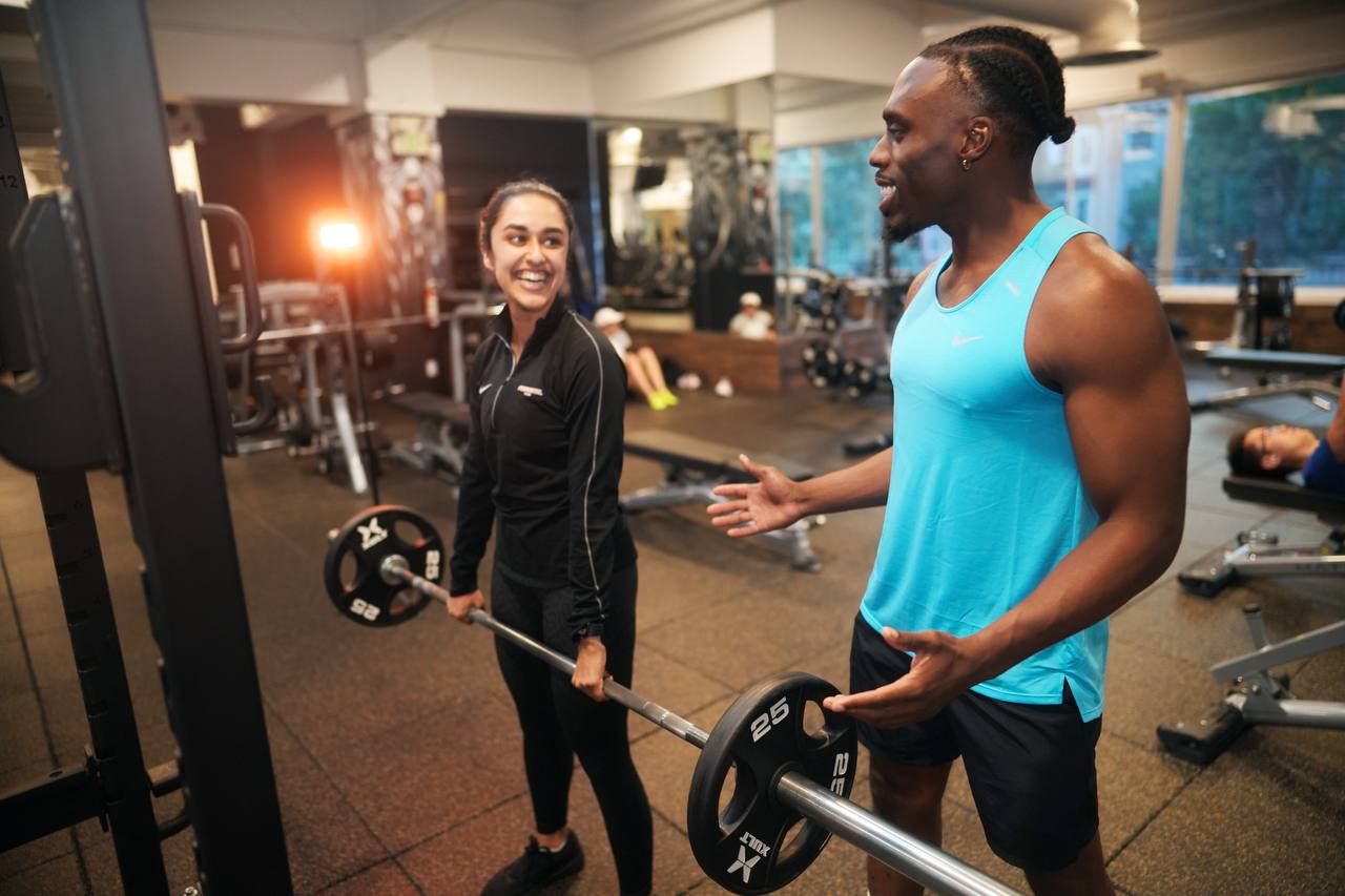 Udoka coaching a client through a barbell lift in the gym