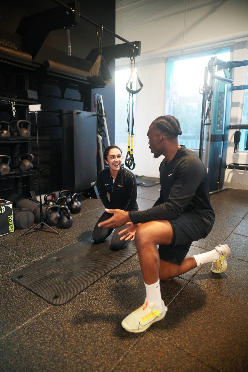 Udoka kneeling on a gym mat, talking a client through a movement