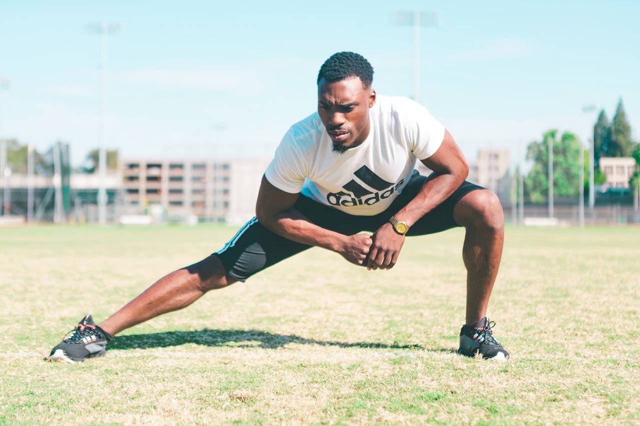 Udoka in a deep side lunge stretch on a sports field